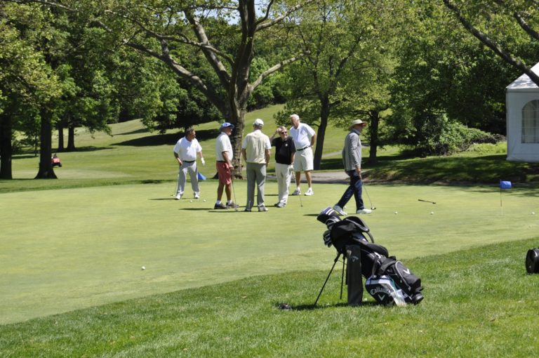 Wide shot golf course of six golfers in the background and a golf caddy in the foreground at the Staten Island Sports Hall of Fame.